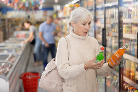 Elderly female customer choosing soft drinks in grocery storeの写真素材