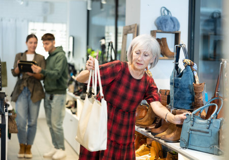 Elderly woman chooses handbag in storeの写真素材