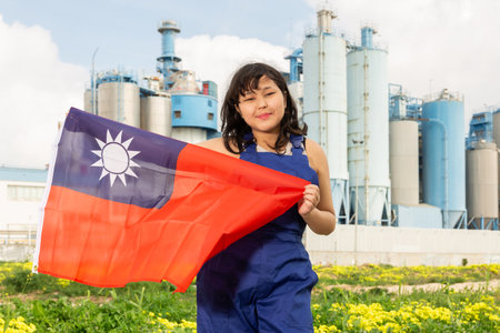 Portrait of positive girl in construction overalls with the Taiwan flag on the background of modern factoryの写真素材