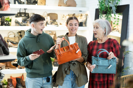 Group of excited shoppers admiring leather bags and wallet in trendy storeの写真素材