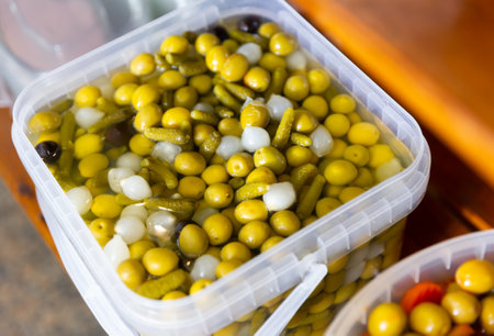 Pickled olives, onion and cucumbers in plastic container on market. Popular vegetarian appetizer closeupの写真素材