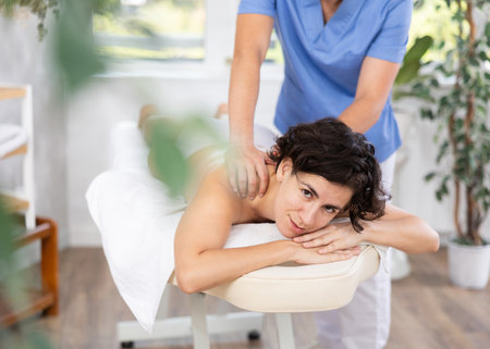 Masseur doing back massage to adult womanの写真素材