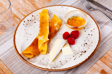 Portion of rolled pancakes with raspberries, honey and pieces of cheeseの写真素材