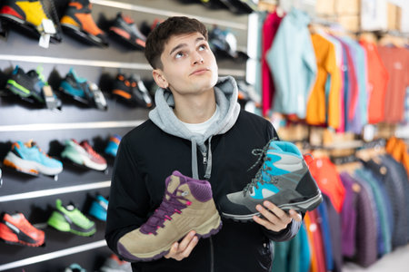 Interested male athlete chooses sports winter shoes for hiking in sports storeの写真素材