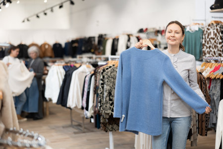 Middle-aged woman choosing convenient jumper in clothing storeの写真素材