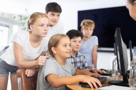 Preteen boys and girls working on computer together with teacher in IT cabinetの写真素材