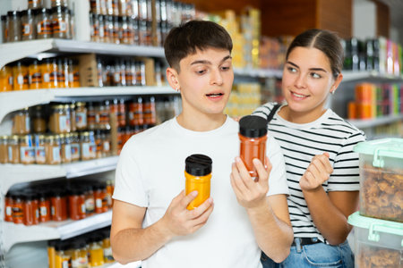 Cheerful young couple choosing spices in glass jars in supermarketの写真素材