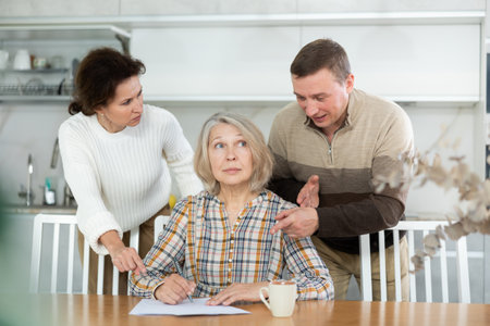 Old woman compiling heritage document while middle-aged man and woman competing in the kitchenの写真素材