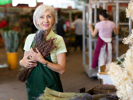 Mature female florist offering bundles of blooming lavender in marketの写真素材