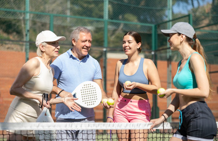 Three women and a man Padel tennis players speaking friendly in the courtの写真素材
