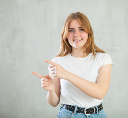 Girl point finger at arm with copy space for promotion over studio wallの写真素材