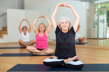 Mature woman making yoga meditation in lotus pose in fitness centerの写真素材