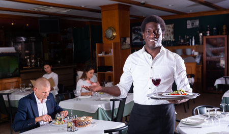 Hospitable african american waiter greeting guests in restaurantの写真素材