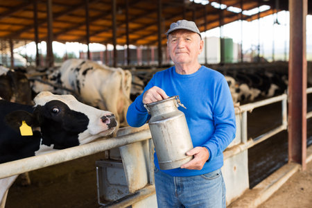 Senior farmer with milk can in cowhouseの写真素材