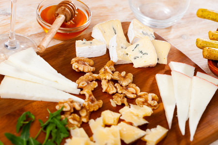 Different types of cheese served on wooden board with honey, slices of walnutsの写真素材