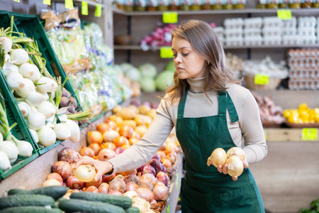 Female seller working in supermarket and lays out onions on counterの写真素材