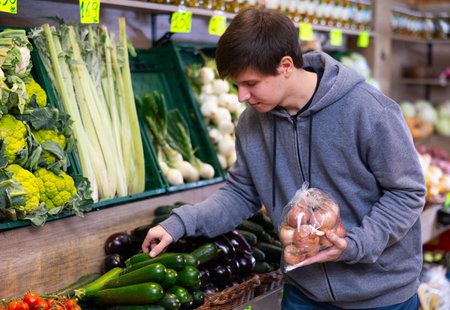 Young guy chooses zucchini in vegetable shopの写真素材
