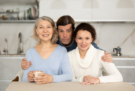 Happy family consisting of man, woman, elderly woman, at home in kitchen