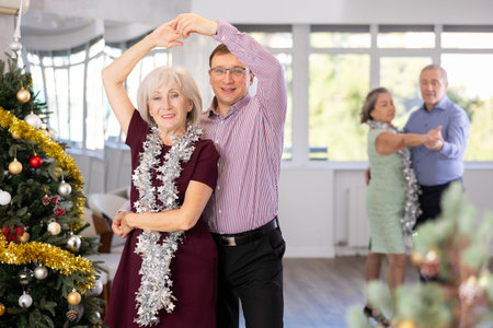 Positive middle-aged man dancing playful Latin dance bachata with mature female partner during celebration Christmas and New Year in choreography studioの写真素材
