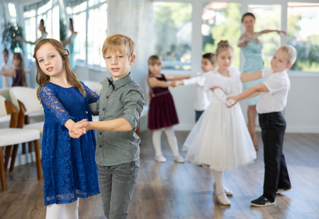 Little children in elegant dresses practicing waltz dance in school hallの写真素材