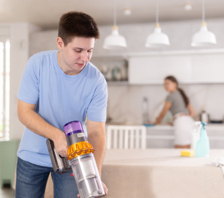 Young guy tidying up apartment, vacuuming kitchen floorの写真素材