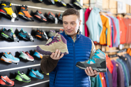 Attentive male athlete chooses sports winter shoes for hiking in sports storeの写真素材