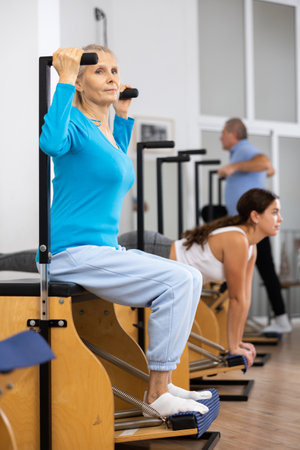 Concentrated mature female practicing Pilates system on Wanda chair machine in studio to improve mobility of upper backの写真素材