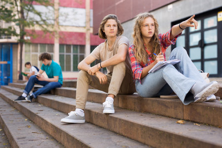 Teenage boy and girl sitting on steps near schoolの写真素材