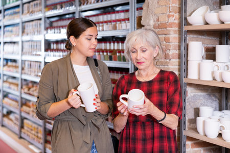 Two women choose mugs or cups together in pottery and ceramics shopの写真素材