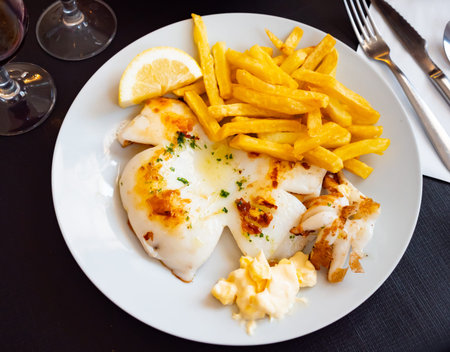 fried cuttlefish drizzled with white garlic and parsley sauce,lemon wedge and french fries on plate