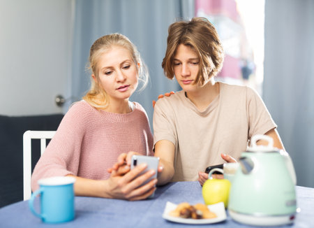Teenager showing pictures on smartphone to interested motherの写真素材