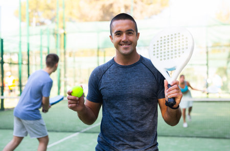 Smiling sporty man standing on outdoor paddle tennis courtの写真素材