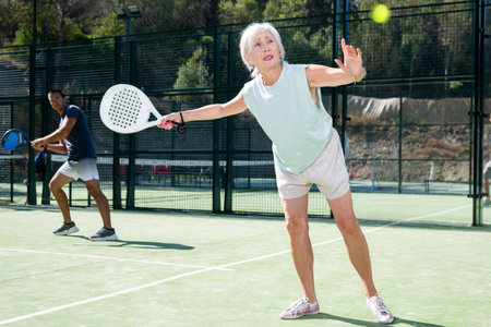 Mature woman playing padel tennis on courtの写真素材