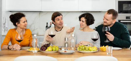 Two married couples are sitting at table, enjoying food and wine, chatting, talking, laughing.