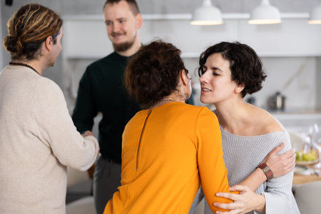 Women hug each other and kiss on the cheek while greeting each other before a festive dinner. Men...