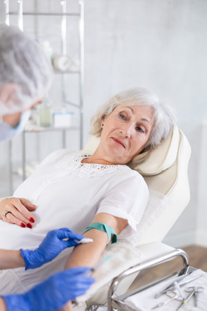 Young doctor drawing blood from elderly patient.の写真素材