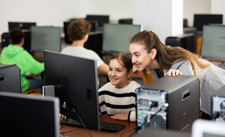 Smiling female teacher talking to happy teenage girl in computer classの写真素材