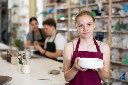 Satisfied teenager girl shows cup created by himself in clay workshopの写真素材