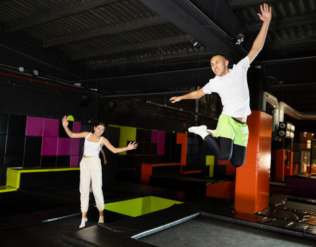Fitness, fun, leisure and sport activity concept - happy man jumping on trampoline indoorsの写真素材