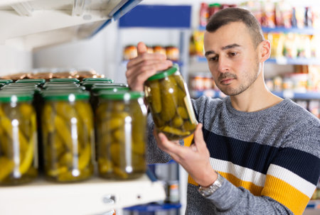 Attentive man buying canned cucumbers at grocery storeの写真素材
