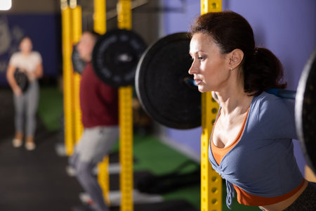Slender woman trains muscles of arms and back using barbell and differentiated weighting in gym