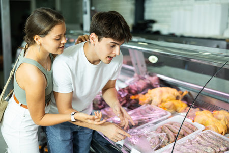 Spouse near butcher shop window inspects goods and choose sausages for grillの写真素材