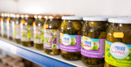 BADALONA, SPAIN - February 12, 2024: Glass jars with pickled tomatoes and cucumbers on the shelves of Russian grocery store in Spainのeditorial素材