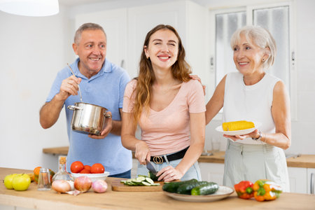 Senior couple spending time together with their adult daughter, cooking delicious meals for dinnerの写真素材