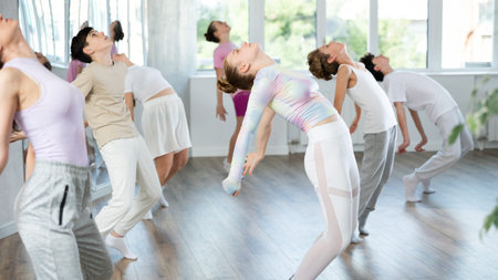 Female girl student repeats movements of unrecognizable teacher during group modern dance class.