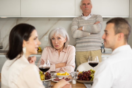 Concerned parents watching adult son communicating with girlfriend at dinner tableの写真素材