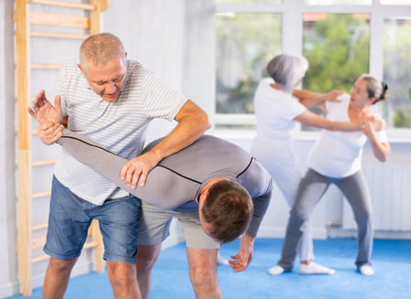 Self defense lesson - elderly man twists the arm of attacking man with painful hold in gymの写真素材