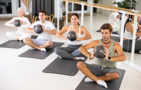 Middle-aged man practicing pilates with ball on gray mat in gym roomの写真素材