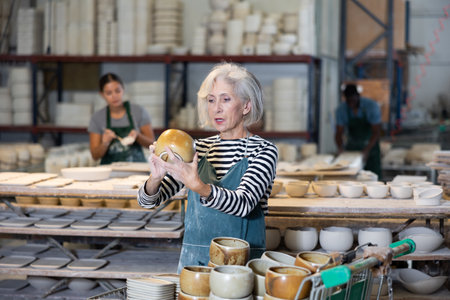 Mature woman ceramist arranging new bowls in workshopの写真素材