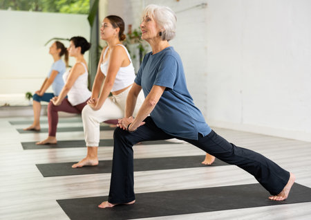 Senior woman maintaining mental and physical health attending group yoga class at studio, practicing stretching posesの写真素材